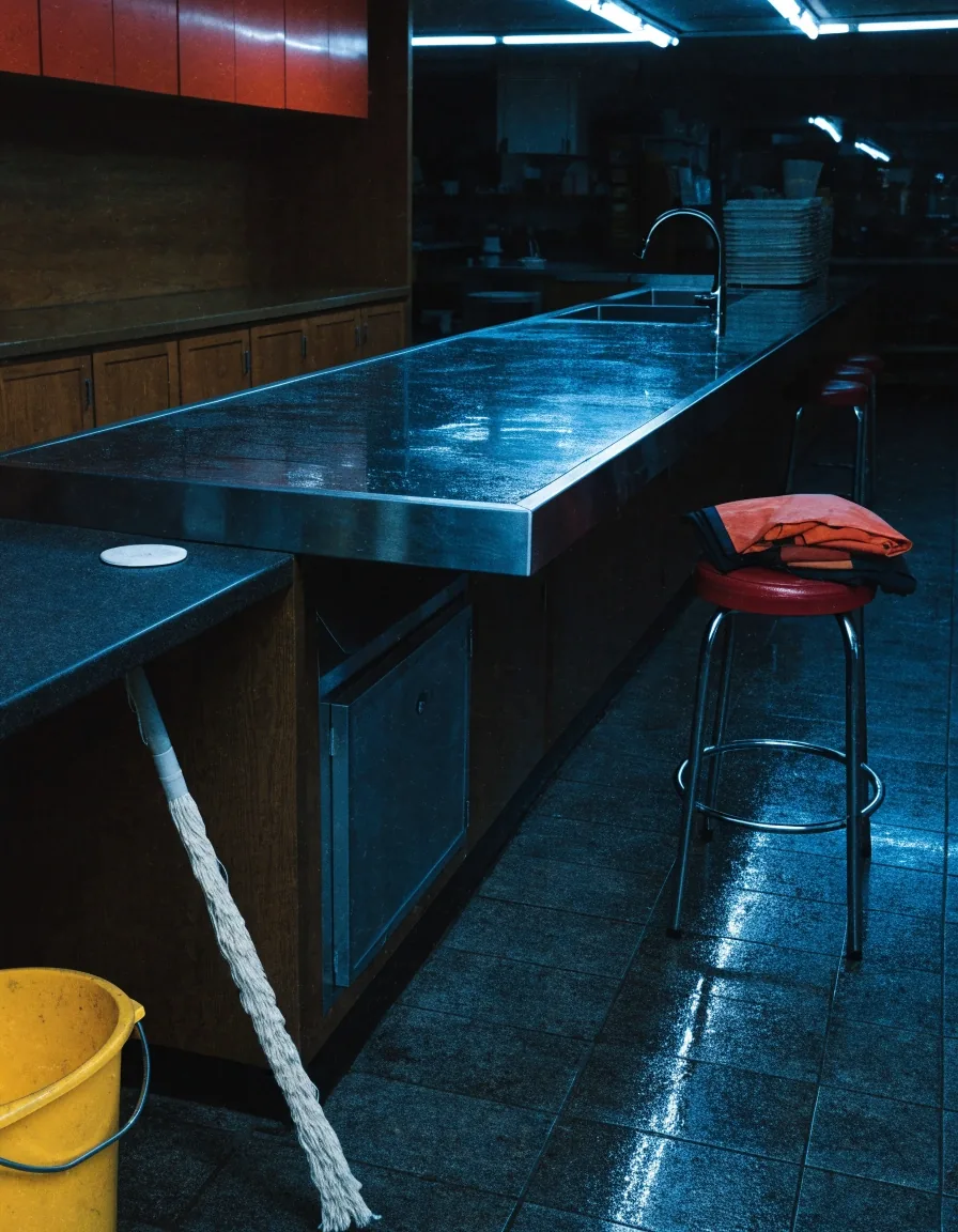Bucket and mop propped at the end of a diner counter with a damp floor and a folded apron on a stool